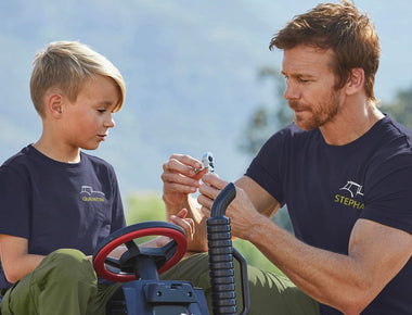 Ein Kind mit einem Mann in gleicher Kleidung, Shirt und Hose - in Teamkleidung. Auf den Shirts der beiden ist das gleiche Logo in ihr Name zu sehen.