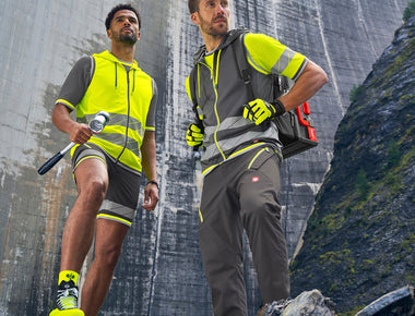 Zwei Herren vor einer Staumauer tragen top sichtbare Warn- und Reflexkleidung aus der Workwear Linie e.s.ambition von STRAUSS.