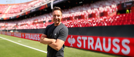 A man with crossed arms standing on a soccer pitch in front of the stands 