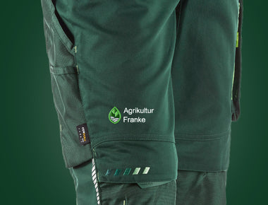 Grüne Arbeitshose mit einem hellgrünen Agrar-Zeichen und dem Schriftzug Agrikultur Franke – auf den Oberschenkel gestickt.