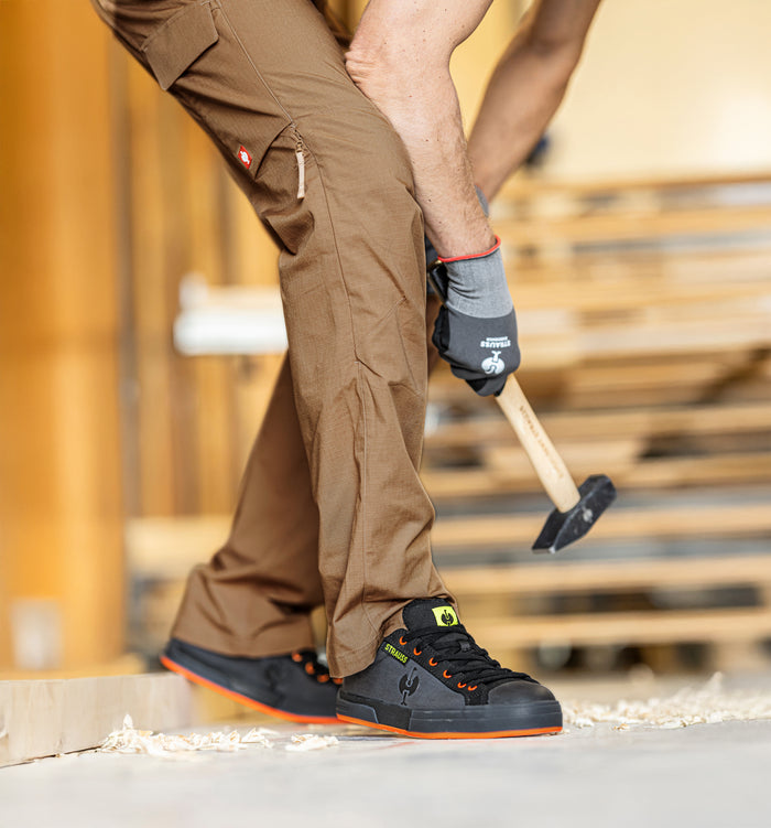 Ein Mann bückt sich mit einem Hammer in der Hand.