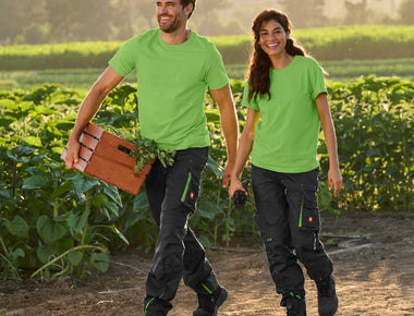 Mann und Frau in Arbeitskleidung mit schwarzen Hosen und grünen Shirts im Sonnenblumenfeld