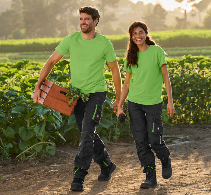 Mann und Frau in Arbeitskleidung mit schwarzen Hosen und grünen Shirts im Sonnenblumenfeld